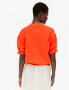 Person wearing an orange sweatshirt with text on the back, standing against a white background
