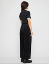 A woman shown from the back wearing a black ribbed short-sleeve cropped top and black wide-leg trousers, standing against a plain light gray studio background.