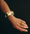 Gold bracelet and ring on a wrist against a black background