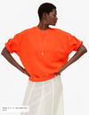 Person wearing an orange sweater with puffed sleeves on a white background