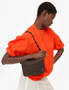 Person wearing an orange top holding a brown woven handbag on a white background