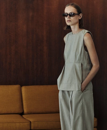 Woman in a light green outfit standing in a room with a brown sofa.