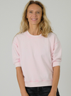 Woman wearing a light pink sweatshirt against a plain background