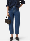 A model wearing a pair of high-waisted, wide-leg cropped blue jeans, paired with a navy blue button-down shirt, black leather loafers, and holding a dark brown handbag against a light gray background.